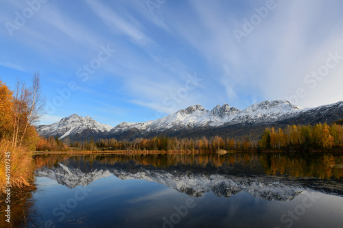 Fall colors, snowy mountains and fluffy clouds reflect in the waters of Alaska's Reflections Lake.