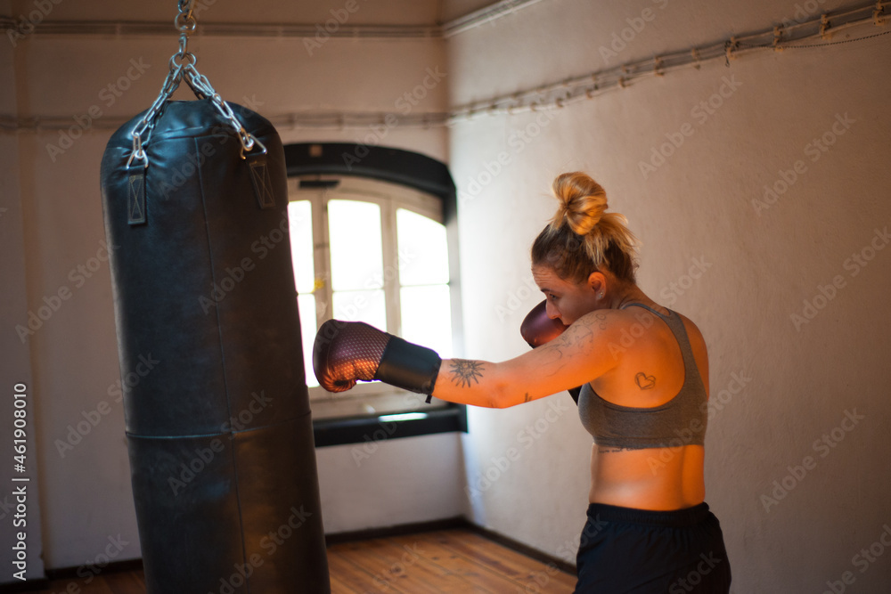 Side view of attractive young woman at kickboxing training. Female boxer hitting huge punching bag at boxing studio. Sport, healthy lifestyle, boxing concept