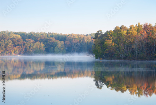 Trees in autumn color on a misty calm lake in northern Minnesota at dawn
