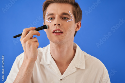 Man applying powder or blushes and doing make-up isolated on blue background