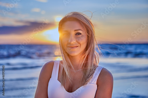 Portrait of european woman who is standing on seaside during sunset and smiling.