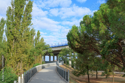 long walkway with trees and sky with clouds and glades and a person in the background