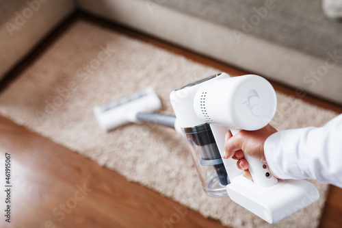 Photography Powerful cordless vacuum cleaner with white cyclonic dust collection technology in hand, cleans the carpet in the house near the sofa