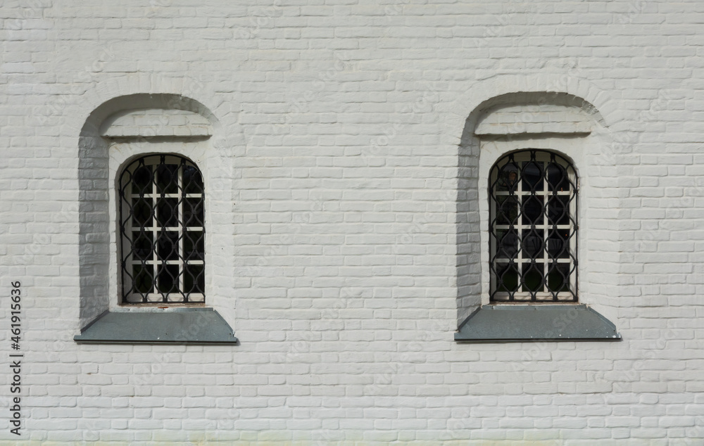 Fragment of the white wall of an old brick building. Traditional Russian architecture. There are two windows with bars. Background. Texture