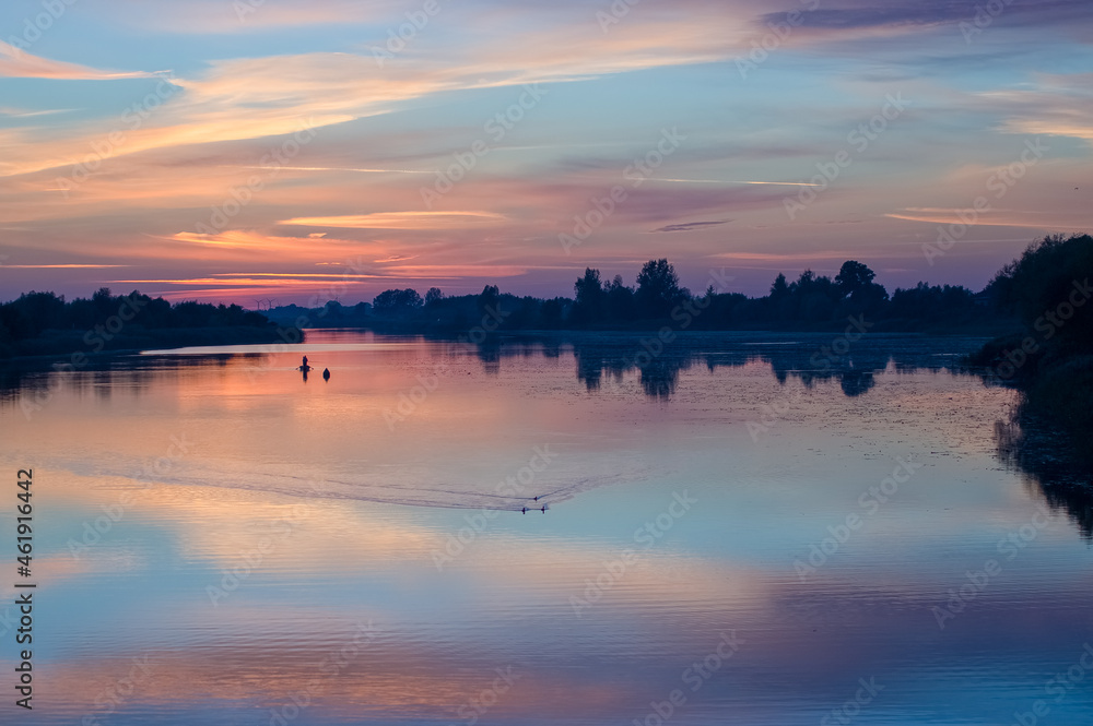 Łódka wędkarze na rzece w pięknym oświetleniu zachodzącego słońca odbicia kolorowych chmur w  wodzie
