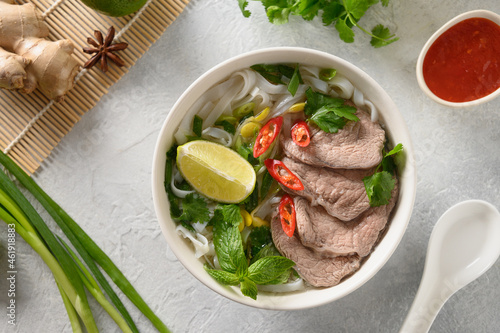 Pho Bo Soup with beef, rice noodles, ginger, lime, chili pepper in white bowl on light backgound. View from above. Close up. Vietnamese and Asian cuisine.