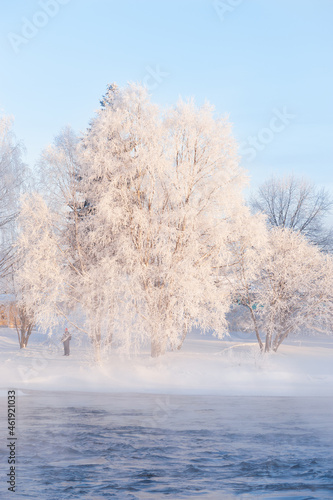 Winter landscape, frost covered trees and mist over freezing river water.