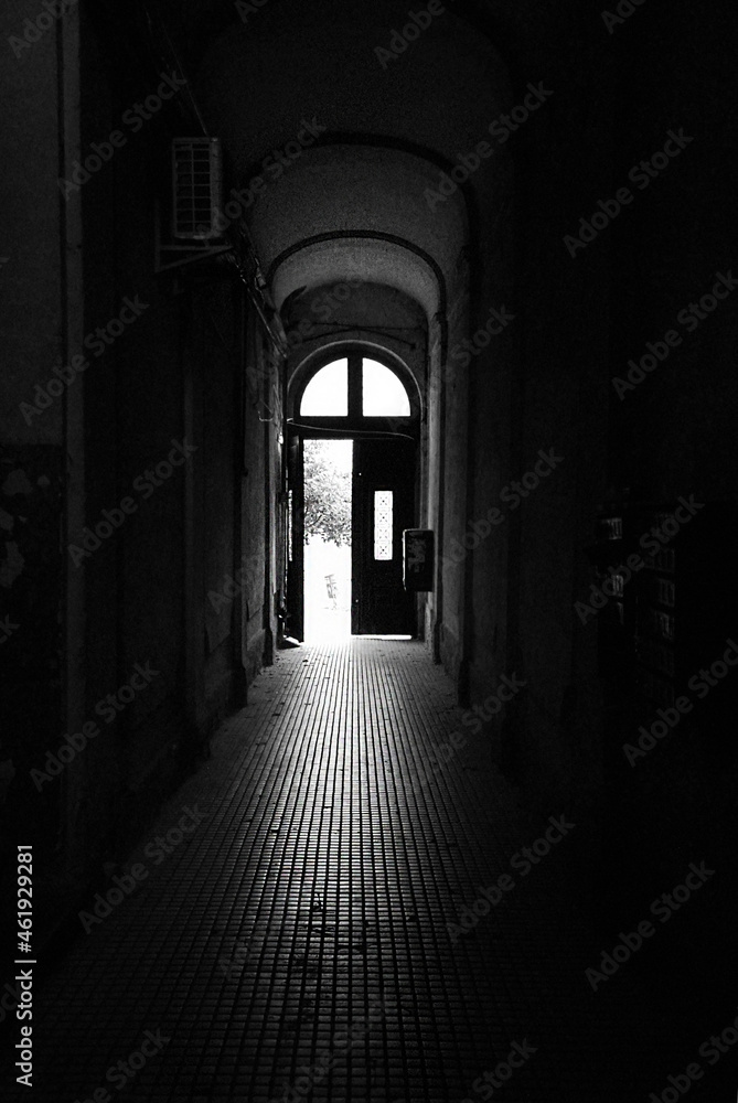 An open door at the end of a long corridor in an old abandoned building. Halloween concept. Monochrome.