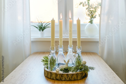 alternative advent wreath, candles in bottles on a wooden board with decoration on a table at the window, two are lit, second sunday before christmas, copy space