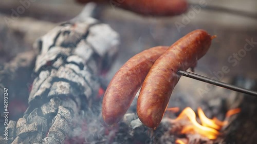 Sausages on a stick cooked over campfire. Outdoor barbecue picnic. Group of people having fast food diner.
