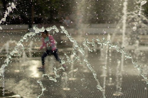 A child runs among the jets of water in the town square. Splashes of the fountain in the summer.