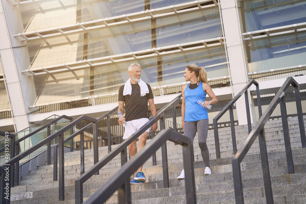 Active sportive mature couple, man and woman in sportswear walking down the stairs after exercising together outdoors