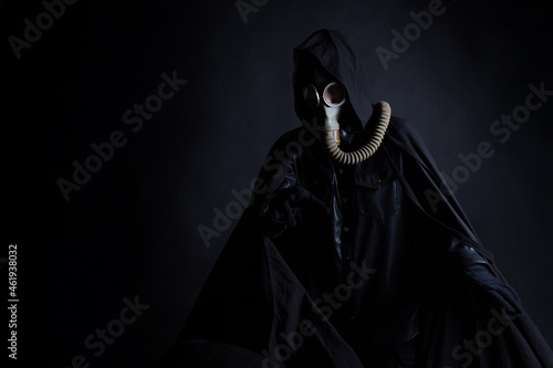 A gloomy man in dark clothes, a black hood on his head, a gas mask protects his face. A character from a post-apocalyptic world, survives in a wasteland, portrait on a black background