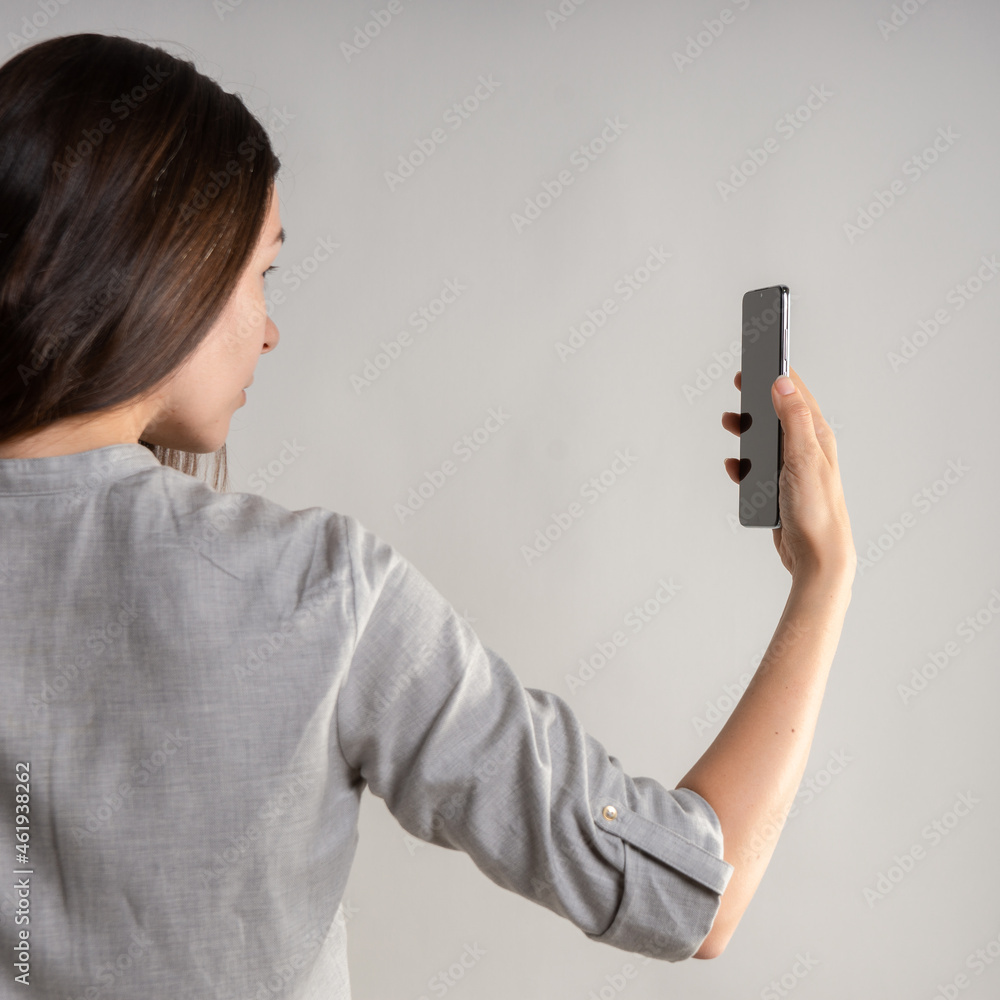 woman holds the smartphone in front of her eyes and unlocks the phone via face id. Face recognition in modern smartphones. Hand gestures, light grey background woman holds the smartphone in front of her eyes and unlocks the phone via face id. Face recognition in modern smartphones. Hand gestures, light grey background