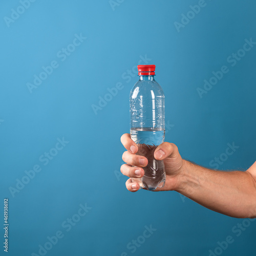 Drink water. A man's hand gives a bottle of clean drinking water. Close-up on a blue background