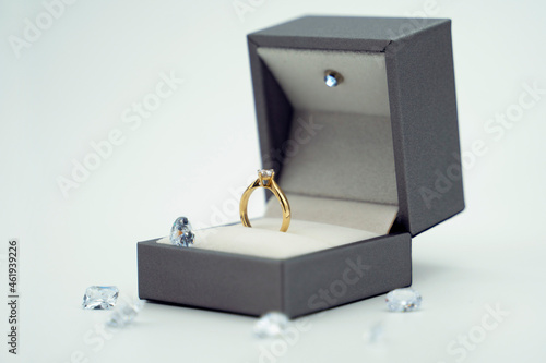 Gold ring in its box, surrounded by diamonds on white background.