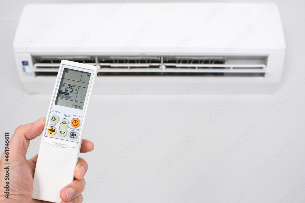 Fototapeta premium Man's hand using remote control open The air conditioner is cooled to 25 degrees Celsius in his bedroom. Health concepts and energy savings
