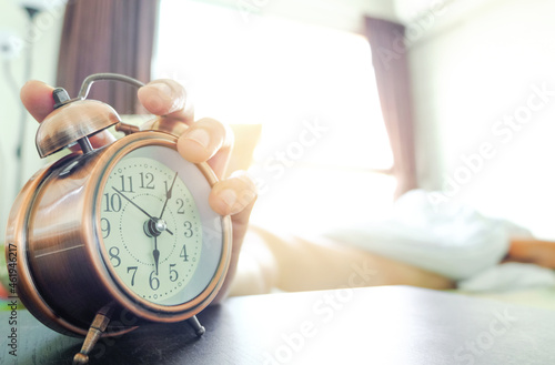 Man sleeping in a bedroom holiday. Hand holding a alarm clock in the morning. concept of health.