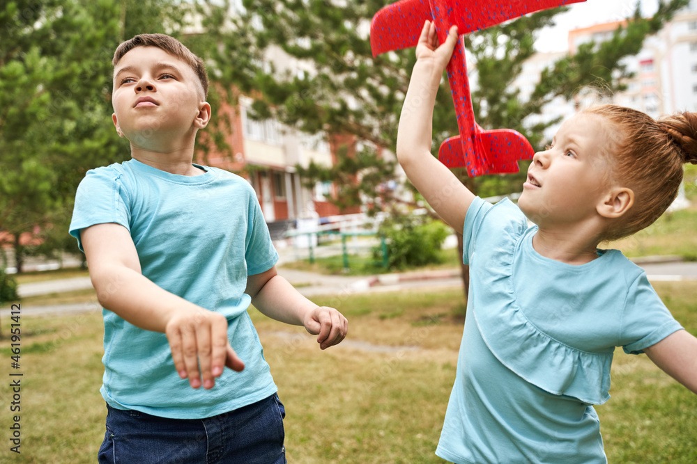 Obraz premium Little girl and boy with airplane toys. Adventure fly concept. Stay home game. Family garden activity. Red hair female portrait. Styrofoam childhood pilot. Summer time. Park outdoor aviation. Siblings