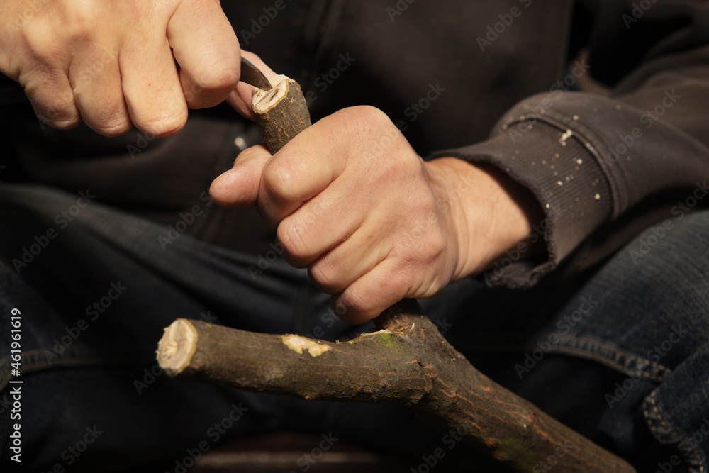 Details of slingshot making of wooden fork by older man in black hooded shirt