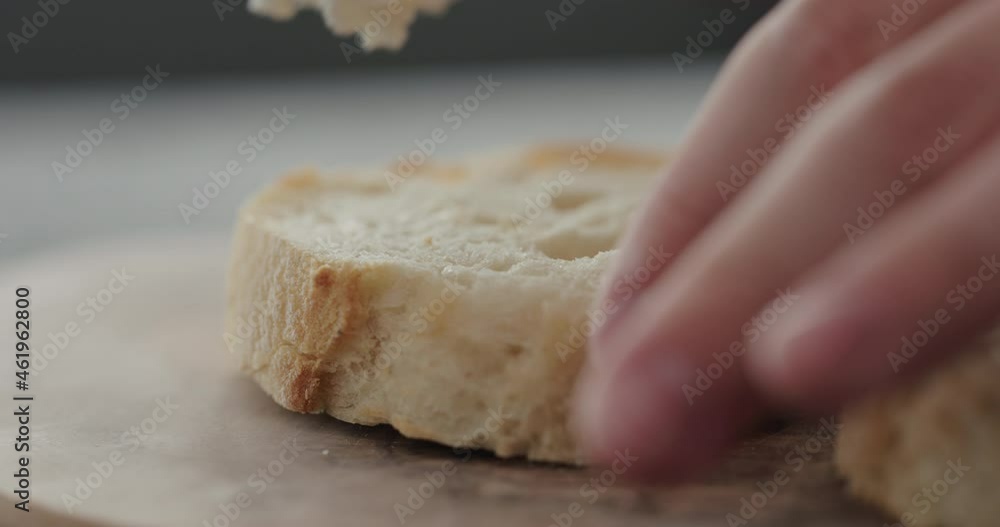 Slow motion spread cream cheese on fresh baguette slice on olive board closeup Slow motion spread cream cheese on fresh baguette slice on olive board closeup