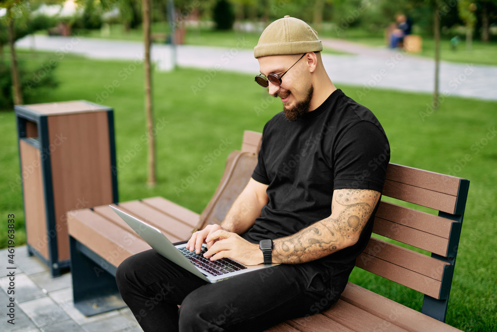 Fototapeta premium Stylish bearded millennial chatting working e-learning laptop at green park Distance education 