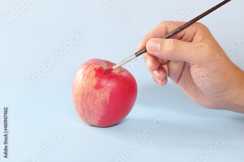 Fake food, coloring, fraud and fraudulent food concept. Hand painting an apple with artificial red colorant or paint.