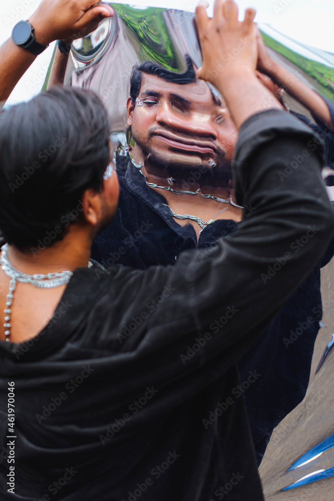portrait of dark skinned Indian man looking into a distorted mirror