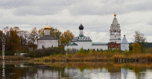 Old Russian Orthodox church lit by the rising sun above autumn forest in light mist reflecting in a pond with a big tree in the foreground