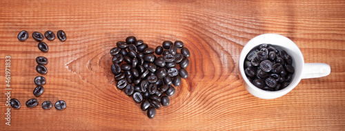 The inscription of coffee beans "I" and a heart made of coffee beans on the background of natural wood with white cup of coffee, banner
