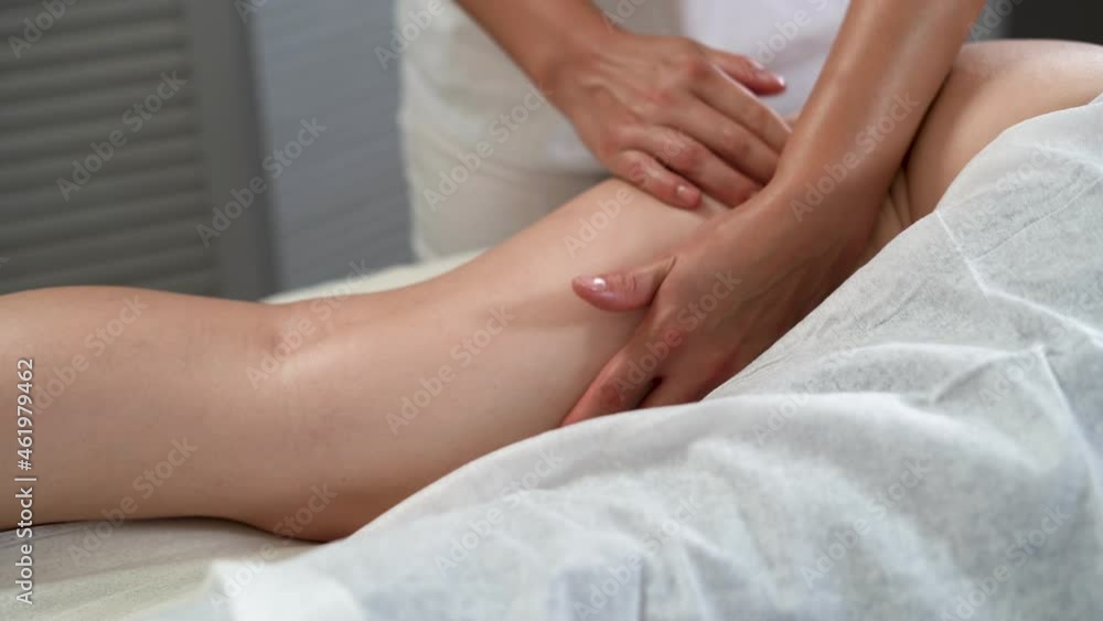 Massage therapist doing anti-cellulite massage of the woman's thigh in the massage parlor. Close-up hands of the master knead the part of the leg. Massage therapist doing anti-cellulite massage of the woman's thigh in the massage parlor. Close-up hands of the master knead the part of the leg.