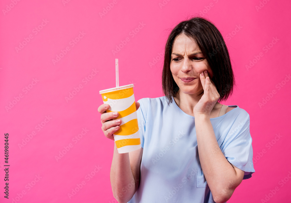 Young woman with sensitive teeth drinking cold water on color background Young woman with sensitive teeth drinking cold water on color background