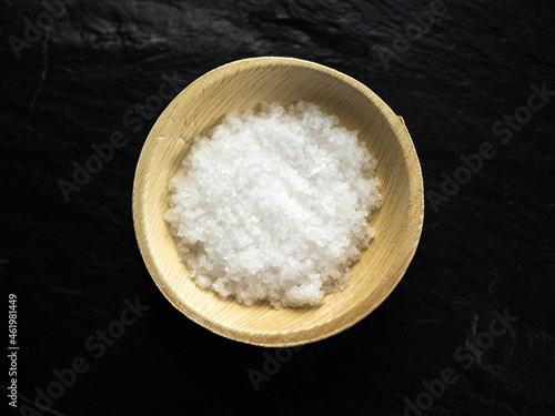 Coarse sea salt in bamboo bowl on slate worktop, background. Flat lay, top view.
