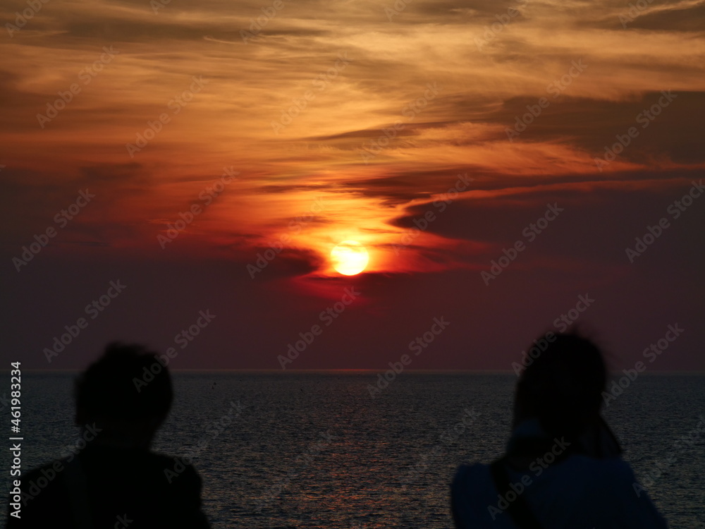 海に沈む夕日と夕焼けの空を見る2人の人影