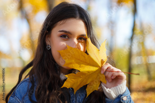 Autumn portrait of a young woman holding a maple leaf in her hand