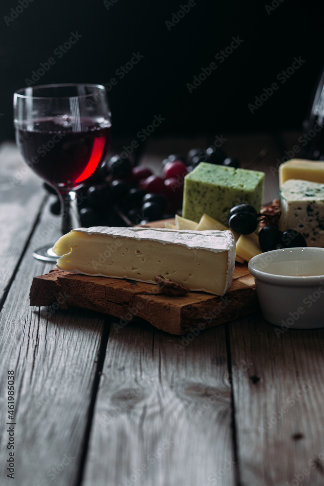 Cheese plate on a dark background. Brie, dor blue, gouda, grapes, nuts, wine