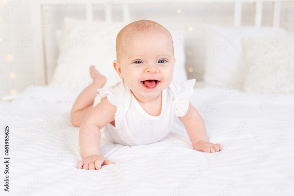 baby girl smiling or laughing lying on her stomach on a white cotton bed at home