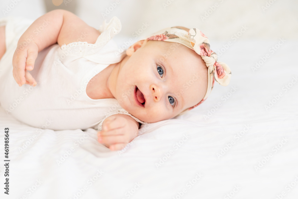 portrait of a baby girl smiling or laughing lying on a white cotton bed at home portrait of a baby girl smiling or laughing lying on a white cotton bed at home