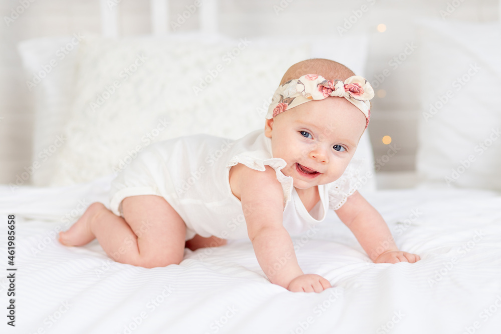 a baby girl smiles or laughs and crawls on her hands on a white cotton bed at home a baby girl smiles or laughs and crawls on her hands on a white cotton bed at home