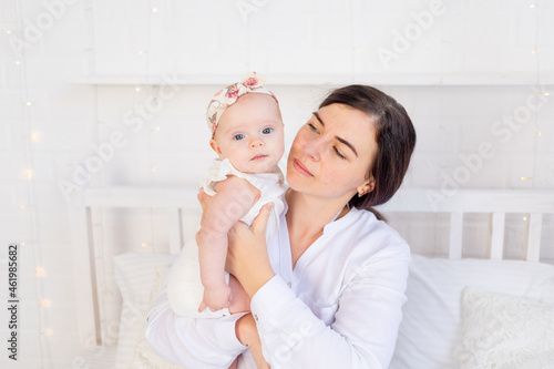 Foto mom anxiously looks at the baby girl on the bed at home, maternal love and care