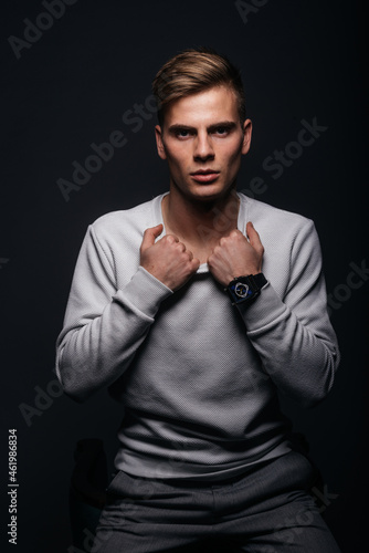 Informally ( casual ) dressed blonde young man with sharp jawline in his 20's posing in a studio in front of a black background while wearing a white sweater. © qunica.com