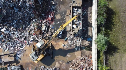 Crane at scrap yard moving scrap metal into a compactor and rubbish compactor is closing when full. Aerial drone top down shot