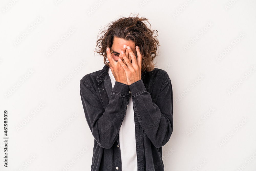 Young caucasian man isolated on white background blink at the camera through fingers, embarrassed covering face.