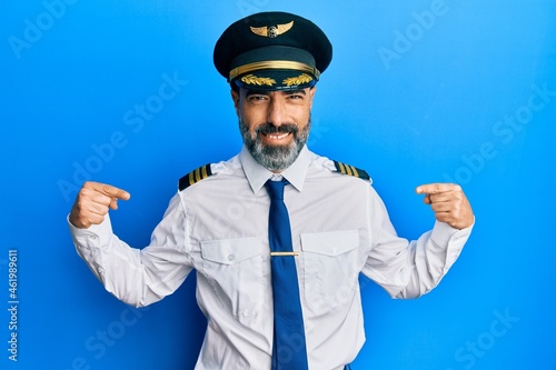 Middle age man with beard and grey hair wearing airplane pilot uniform looking confident with smile on face, pointing oneself with fingers proud and happy.