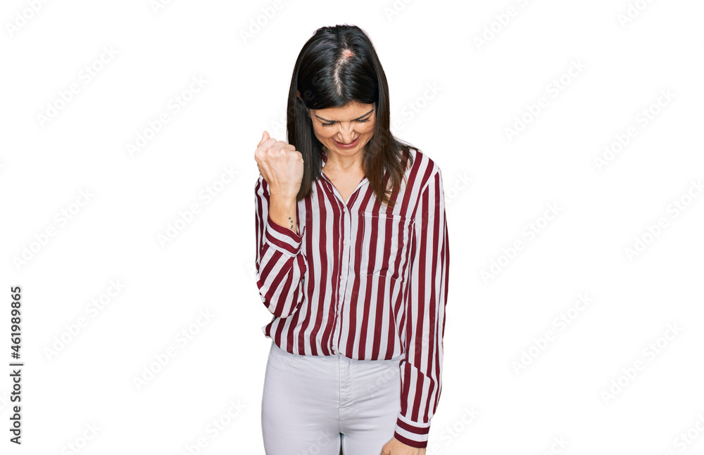 Beautiful brunette woman wearing striped shirt angry and mad raising fist frustrated and furious while shouting with anger. rage and aggressive concept. Beautiful brunette woman wearing striped shirt angry and mad raising fist frustrated and furious while shouting with anger. rage and aggressive concept.