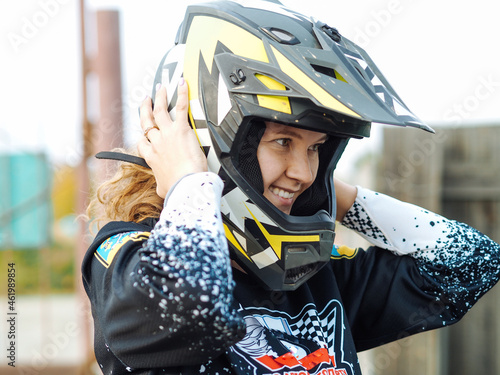 Fototapeta Naklejka Na Ścianę i Meble -  young woman with curly hair smiling in helmet and  protective gear for motocross