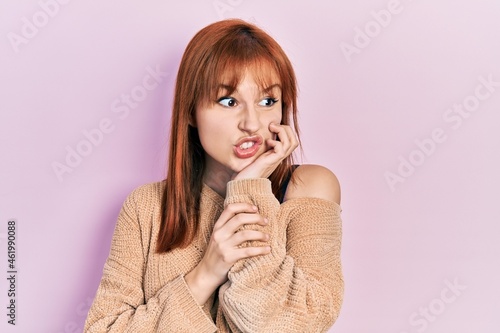 Redhead young woman wearing casual winter sweater looking stressed and nervous with hands on mouth biting nails. anxiety problem.