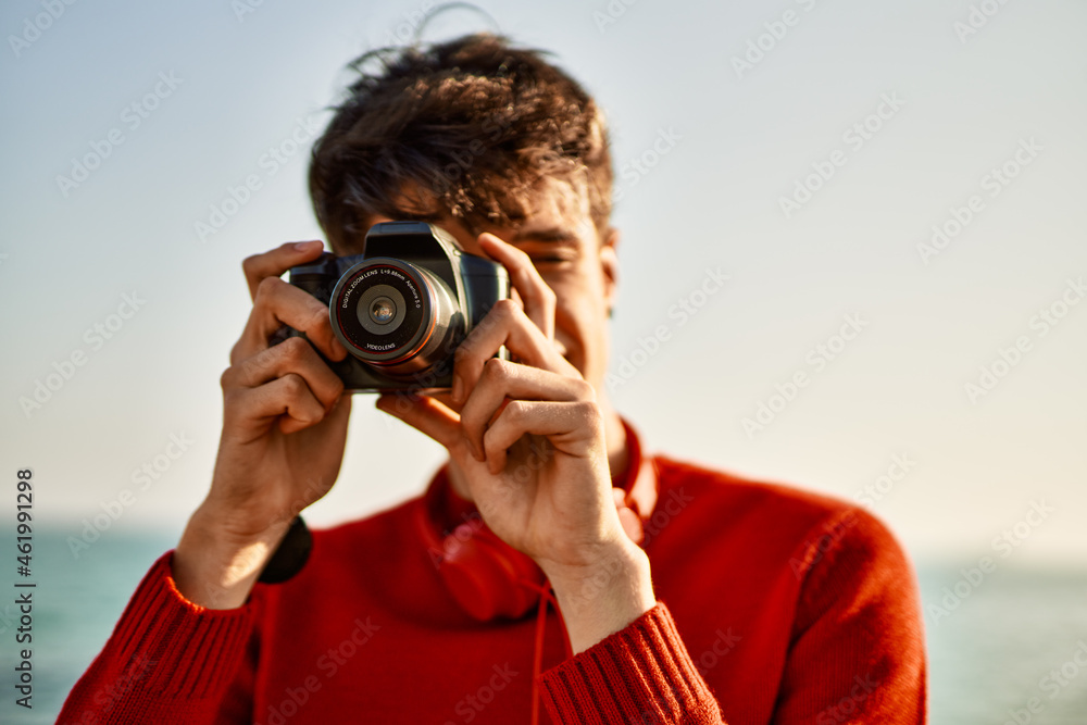 Young hispanic man smiling happy using reflex camera at the beach