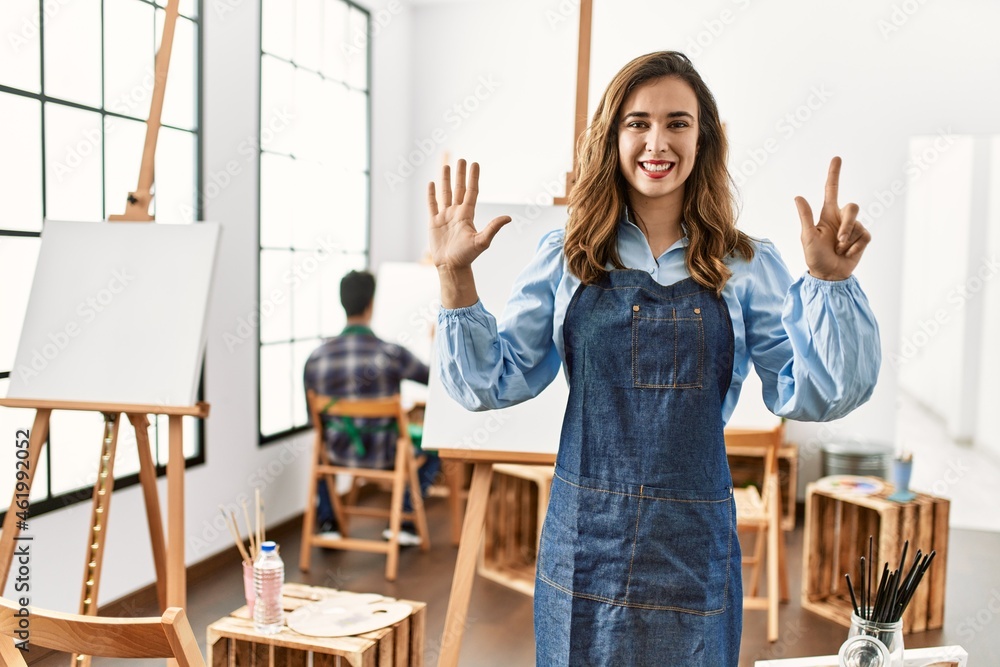 Young artist woman at art studio showing and pointing up with fingers number seven while smiling confident and happy. Young artist woman at art studio showing and pointing up with fingers number seven while smiling confident and happy.