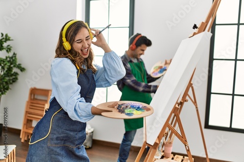 Two hispanic students smiling happy painting at art school. Standing and dancing with smile on face.